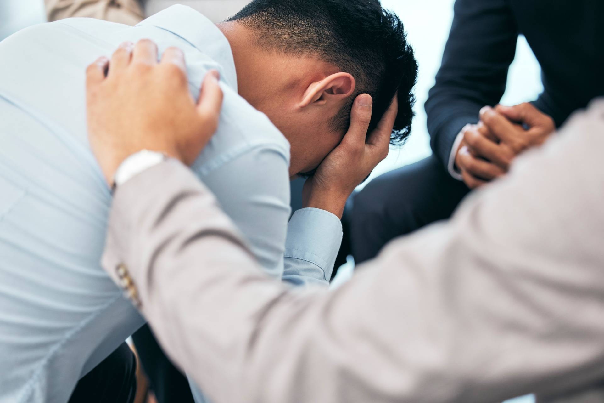 Depressed man sitting while supportive peers offer comfort and encouragement in a wellness center setting.